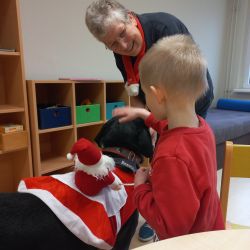 Ein kleines Kind Streichelt einen Hund der einen Kleine Weihnachtsmann auf seinem Rücken trägt.