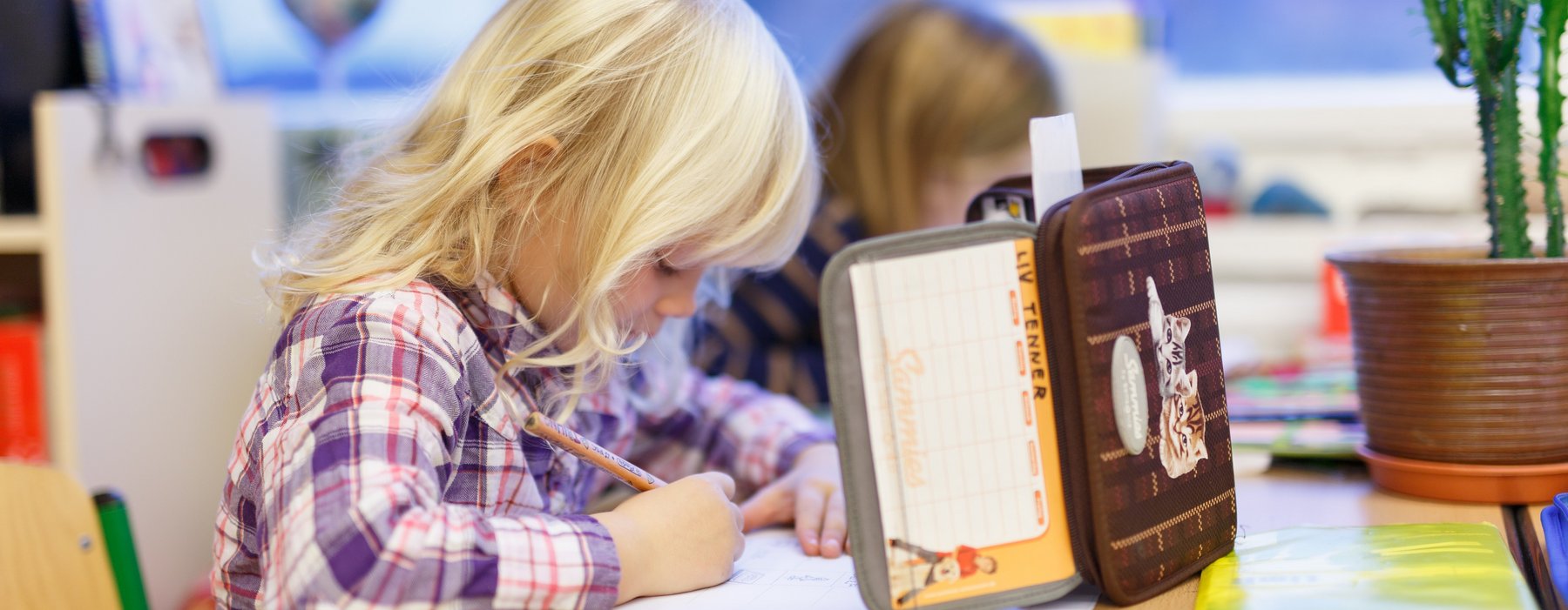 Ein Kind was an einem Schultischsitz mit einer Federmappe als Sichtschutz