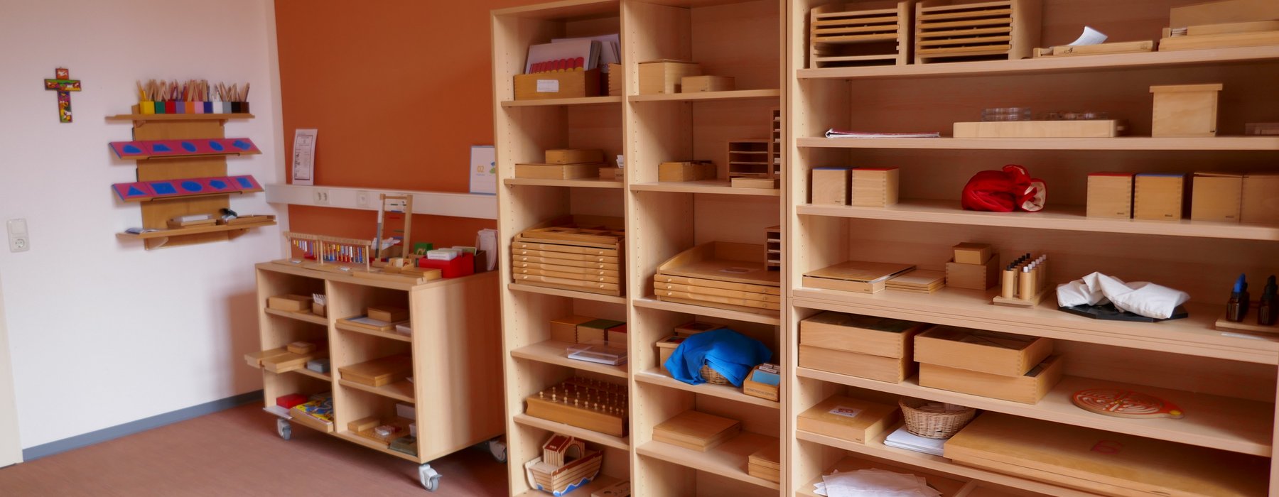Ein Blick auf eine Wand an der auf der Rechten Seite Zwei Große Holzregale stehen die über die hälfte der Wand abdecken. In diesen regalen sind die verschiedensten Holzboxen und Holzkonstruktionen die von den Kindern gebaut werden.