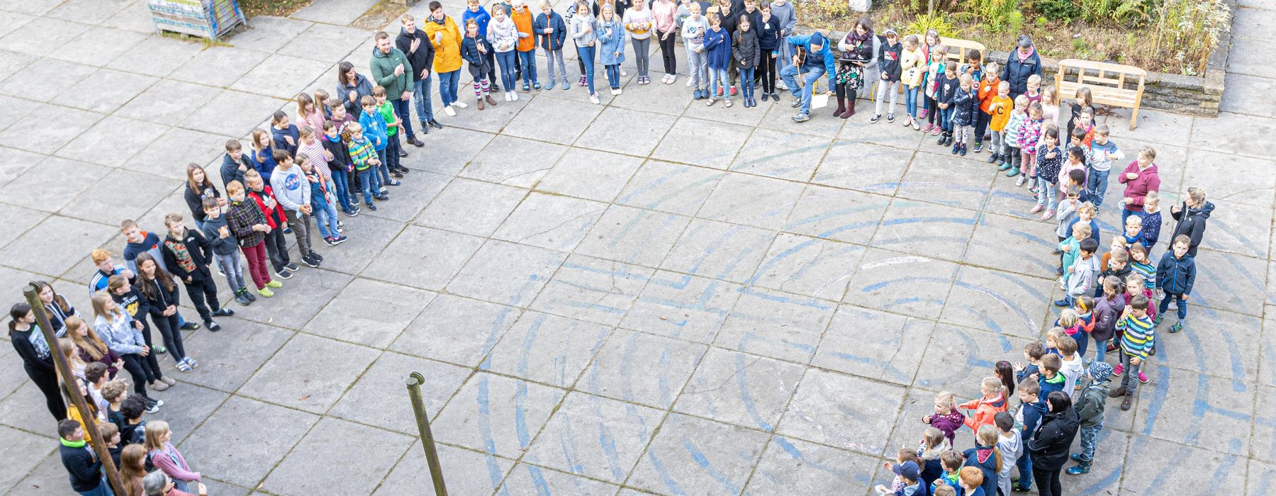 Eine große Ansammlung von Schülern steht auf dem Schulhof in einem kreis in der Mitte ist ein großer Freiraum