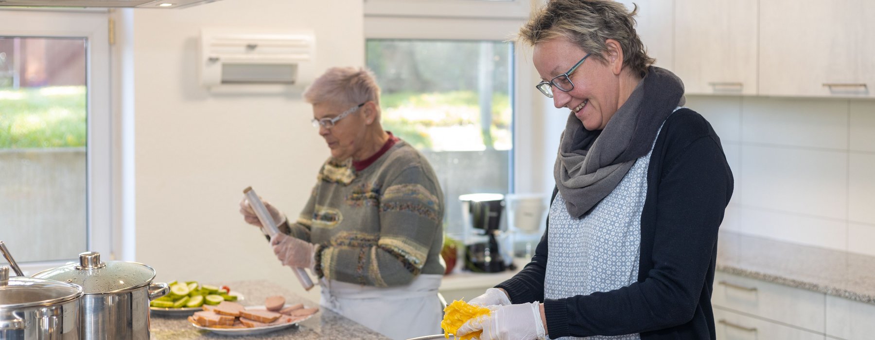Zwei Leute Kochen eine Person schneidet eine Paprika die andere versucht Frischhaltefolie abzuziehen.