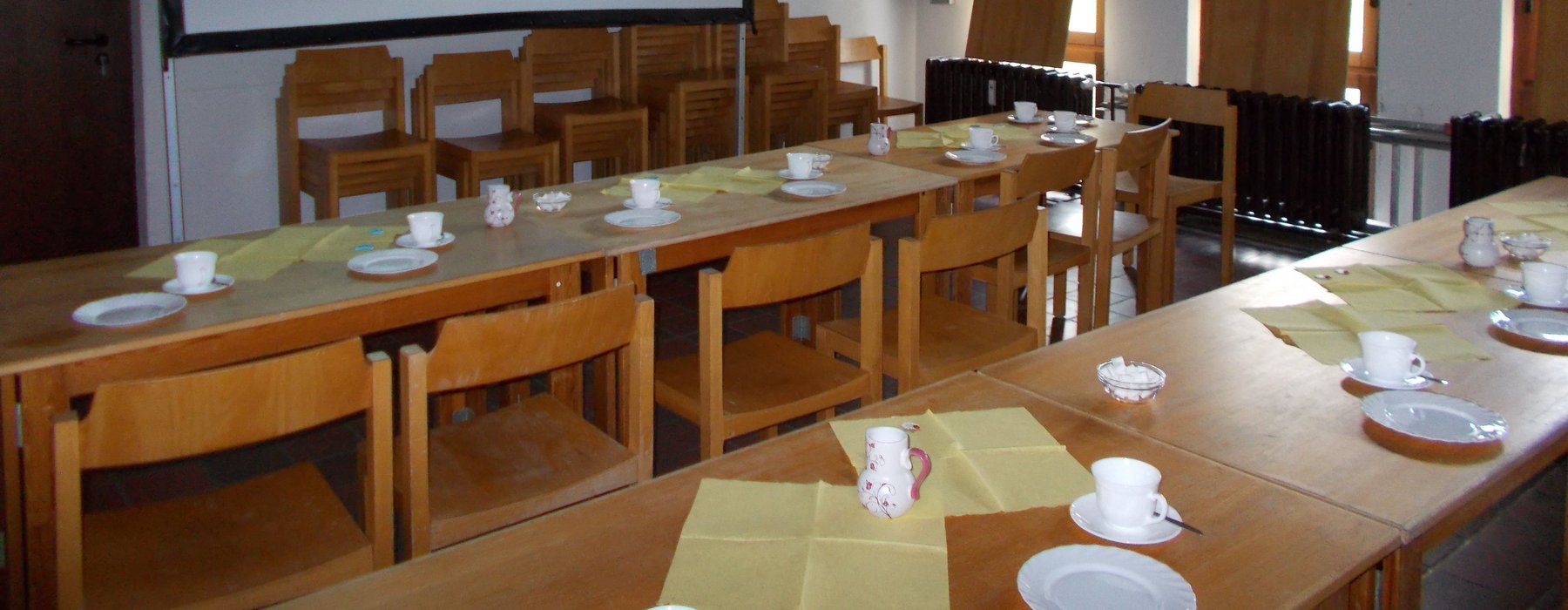 Holztische und Holzstühle für eine große Anzahl von Leuten. Die Tische sind für Kaffee eingedeckt